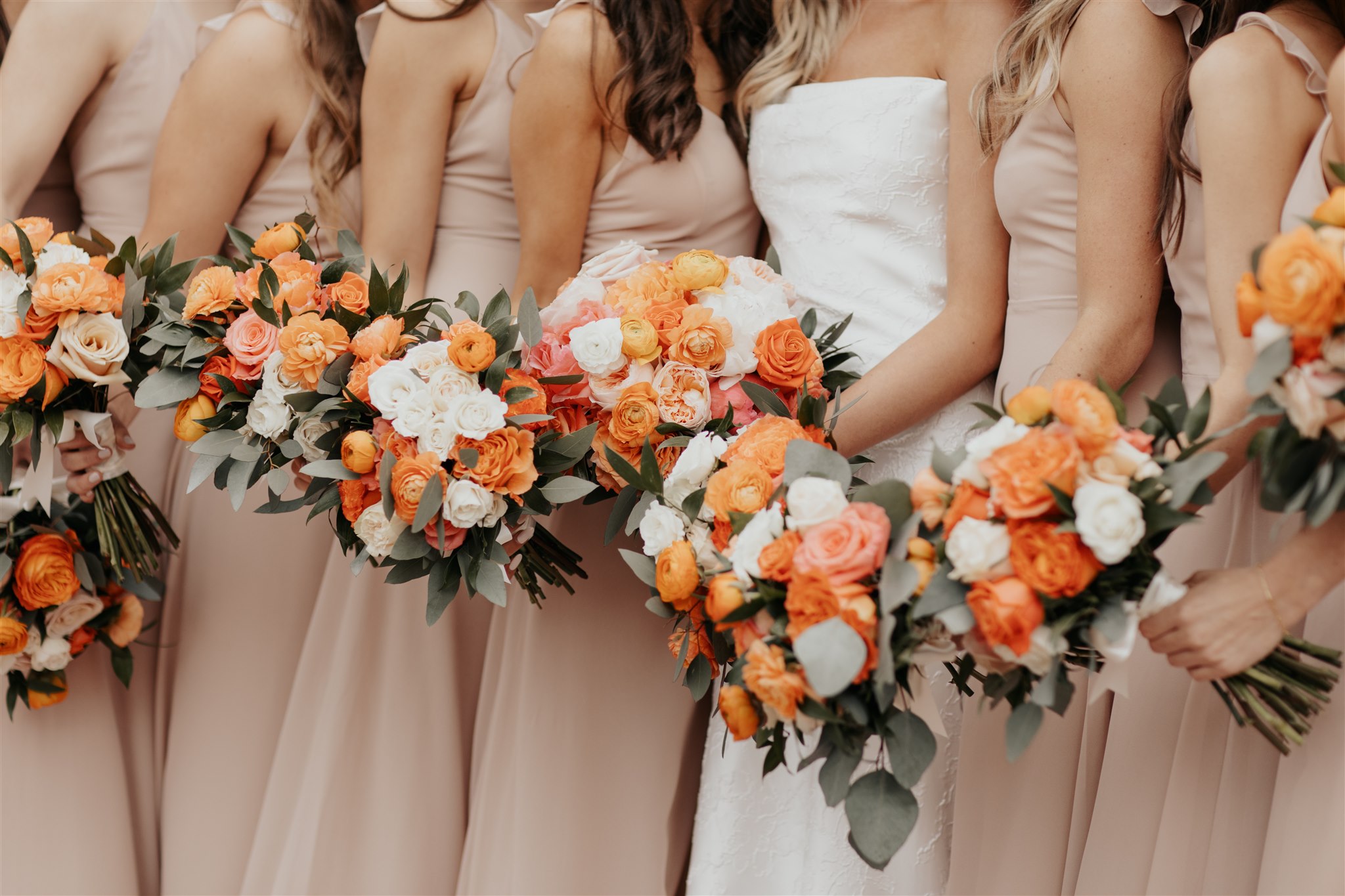 Bride and bridesmaids holding orange, peach and white rose bouquets in blush dresses at Villa Antonia wedding