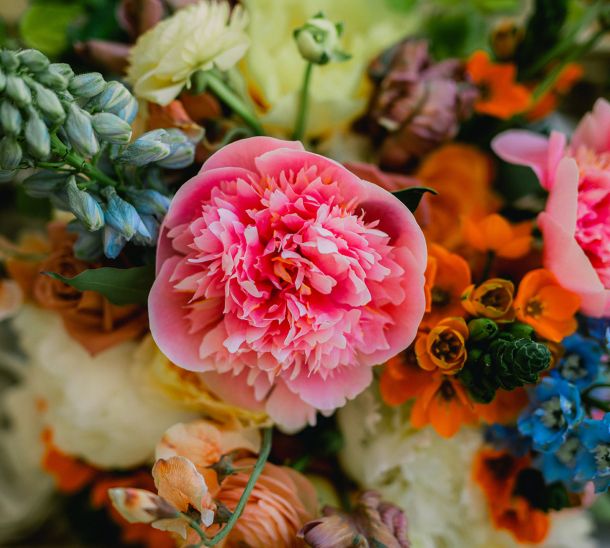 Close-up of a colorful wedding bouquet with pink peonies, orange blooms, and blue accents at Wishwell House
