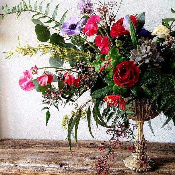 In The Garden floral arrangement with red roses, pink and purple blooms, greenery, and succulents in a pedestal vase