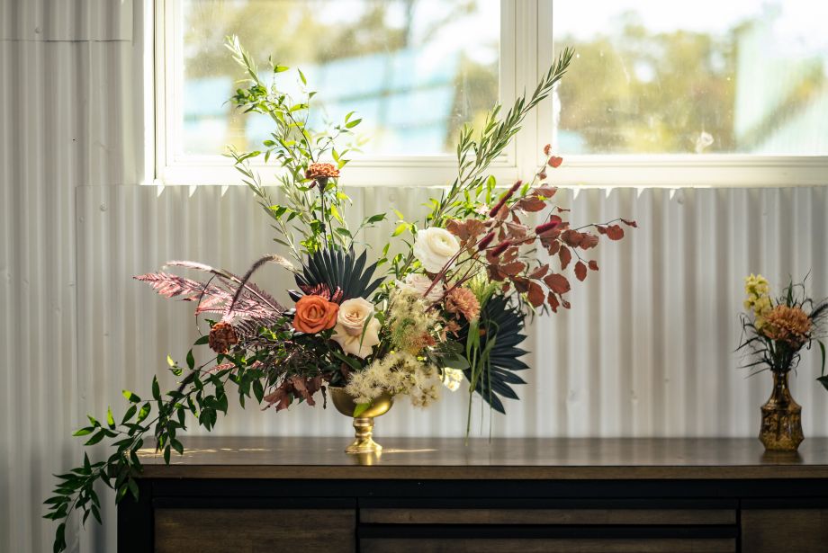 Floral arrangement with roses and greenery in a gold vase on a table by a sunlit window at Dove Nest Estate