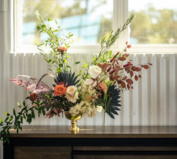 Floral arrangement with roses and greenery in a gold vase on a table by a sunlit window at Dove Nest Estate