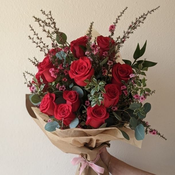 Wrapped bouquet of a dozen red roses with greenery and small pink filler flowers