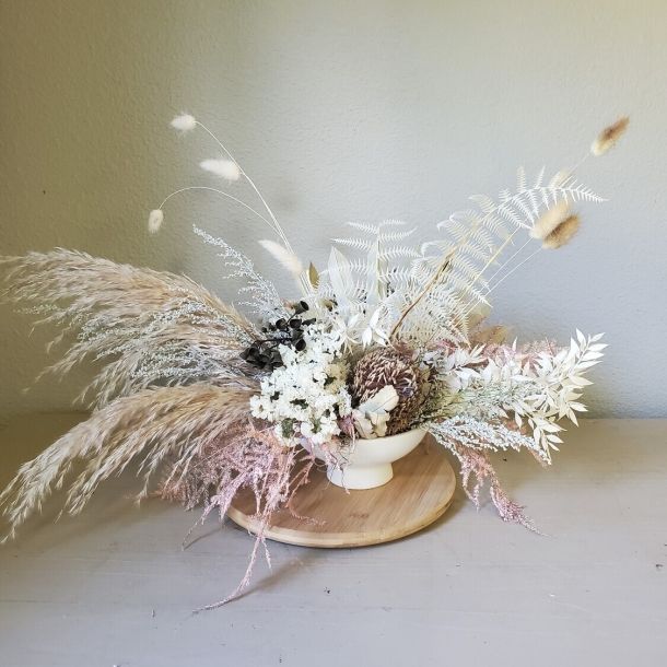 Alma dried floral arrangement in a white bowl with pampas grass and neutral-toned foliage on a wooden board
