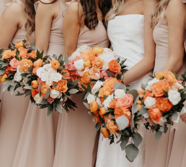 Bride and bridesmaids holding orange, peach and white rose bouquets in blush dresses at Villa Antonia wedding