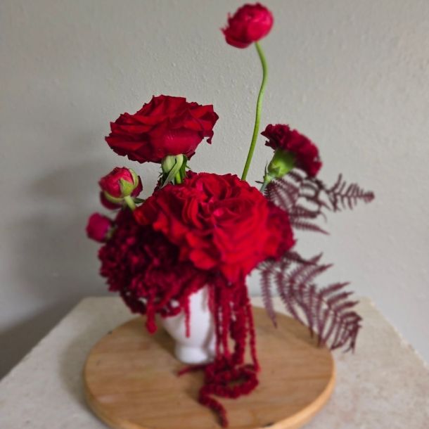 Emma floral arrangement with red blooms in a white vase on a wooden stand